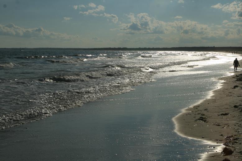A woman with a large full lenth mumu walks the beach as a silhouette in the late day.  The sparkling effect of the light on the waves creates a visual spectacle.  The joy in the picture is that there are many silhouttes walking in the lateday glow of magical light.