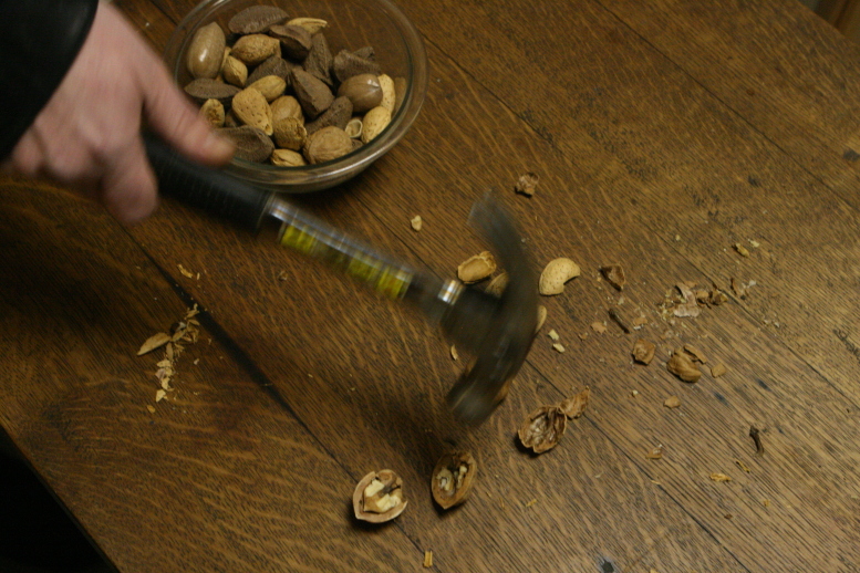 Hammer in motion over a dark stained antique oak desk on a Winter's day 2011.  There are various cracked nuts on the desktop:  Walnuts, Almonds, and various shells.