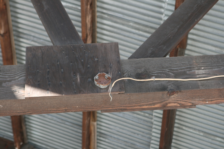 Hanging wire beneath an open roof of a giant warehouse structure next to an abandoned 4 inch diameter (estimated) electrical box, copyright © 2011